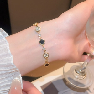 Macro detail of elegant gold flower bracelet with black enamel and zircon pavé charms