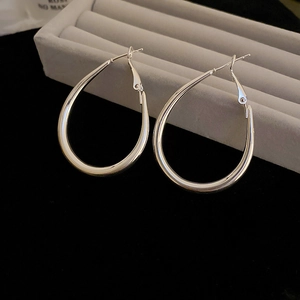 Close-up of silver geometric teardrop hoop earrings on a velvet jewelry display stand
