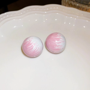 Macro shot of pink and white marble texture bead earring on white wavy plate