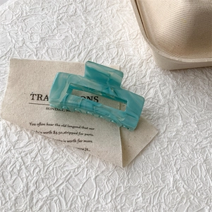 Detail of square turquoise acetate claw clip with water ripple pattern on canvas