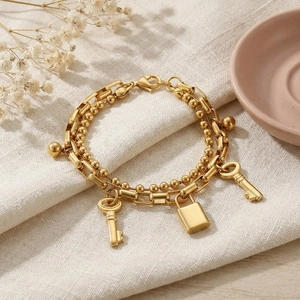 Close-up of double-layer gold chain bracelet with padlock and key charms on linen fabric