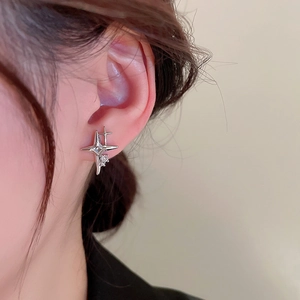 Macro detail of a sparkling silver four-pointed star stud earring on a model ear