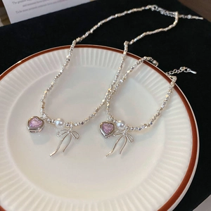 Detail of silver pearl necklaces with pink heart and bow pendants on a ceramic plate