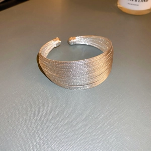 Detalle macro de un brazalete abierto multicapa de hilo tejido plateado con brillo