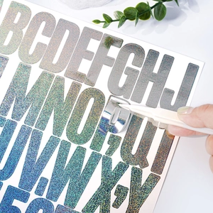 Detail of laser glitter alphabet stickers being applied with tweezers for DIY crafts