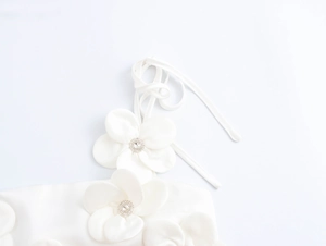 Detailed close-up of 3D fabric flower with rhinestone center on white crop top strap