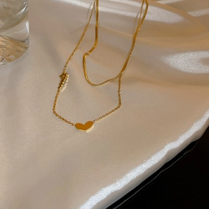Dettaglio di una collana dorata a due strati con pendente a cuore su tessuto di raso