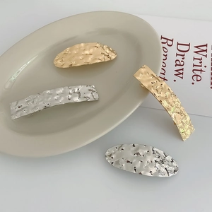 Detail of gold and silver metal hair clips with irregular hammered texture on a tray