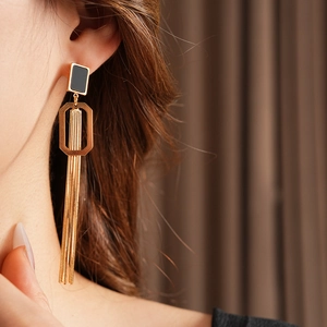 Détail de boucles d'oreilles géométriques dorées avec clous carrés noirs sur un mannequin