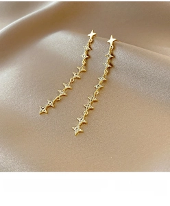 Macro shot of gold-plated star tassel earrings with zircons on champagne satin fabric