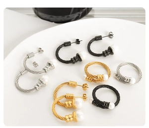 Detail shot of twisted wire earrings and rings in gold, silver, and black with pearls