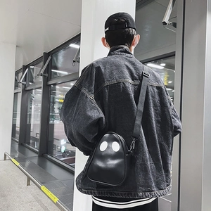 Close-up of black ghost crossbody bag with eye details on casual denim jacket outfit