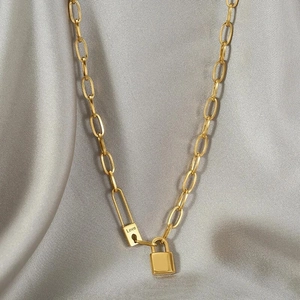 Golden chunky chain necklace with Love pendant and padlock on grey fabric background