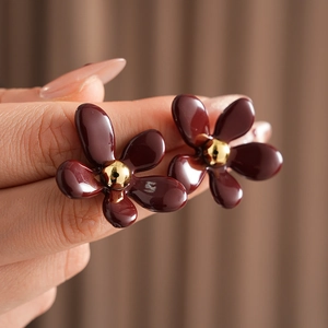 Detail showing hand-held dark red floral earrings with metallic center and vintage design