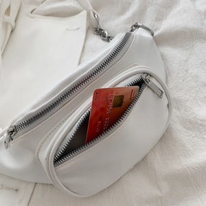White faux leather waist bag with silver chain and adjustable strap on white fabric