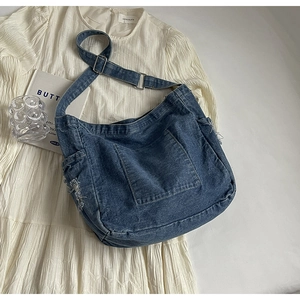 Détail du sac bandoulière en denim bleu avec bords effilochés et boucle métal