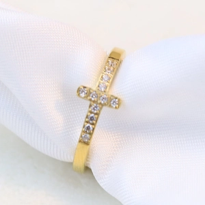 Close-up of gold cross ring with inlaid white zircons on a white silk background