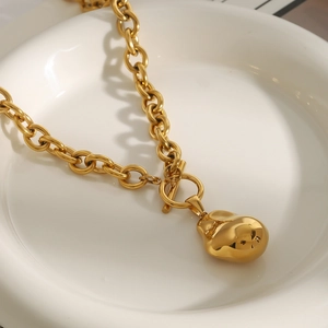 Dettaglio della collana a catena dorata con pendente irregolare su vassoio in ceramica