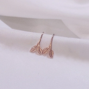 Elegant rose gold leaf stud earrings with detailed nature veins on white fabric