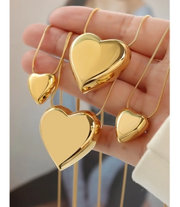Close-up of heart-shaped gold pendants in various sizes held by hand for scale