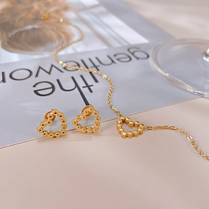 Détail d'un ensemble de bijoux coeur doré avec collier et boucles sur fond rose