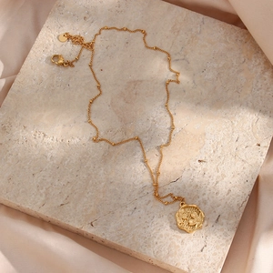Detail view of gold cherry blossom pendant on a bead chain over textured stone