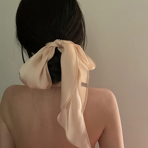 Detail of a large champagne silk bow hair tie with long ribbons on a ponytail