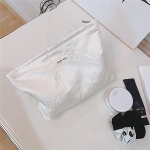 Detailed view of white jacquard toiletry bag with simple wish label on white desk
