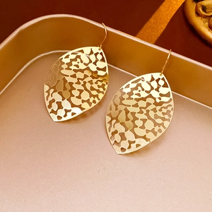 Detail shot of hollow leaf gold earrings on a matching metal tray texture