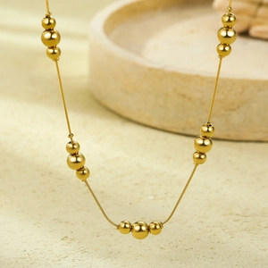 Minimalist golden stainless steel bead necklace with multi-size spheres on a stone surface
