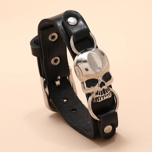 Detail shot of a black leather bracelet featuring a polished silver metal skull charm