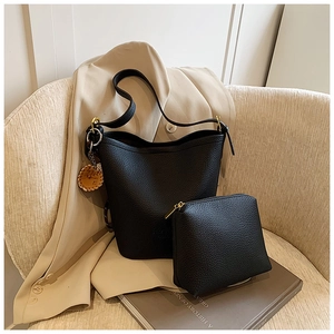 Close-up of black lychee-patterned bucket bag and small pouch set on a soft chair