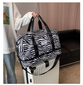 Détail du sac de voyage zébré avec deux poignées et sangle sur une valise blanche