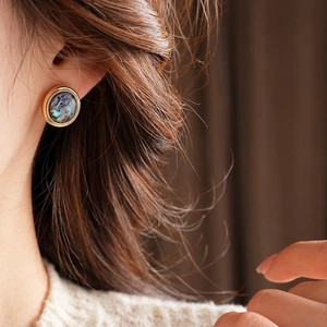 Close-up of 18K gold plated earring with dark shell inlay worn on a model ear