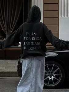 Detailed back view of oversized black hoodie with silver letter print in city street setting