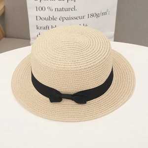 Close-up of beige straw sun hat with black ribbon bow on a clean white desk surface