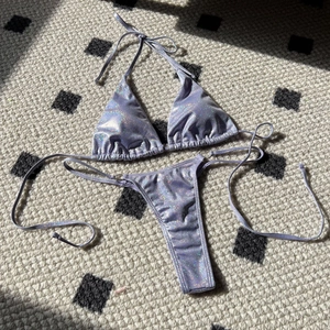 Flat lay of light purple glitter bikini with shimmering laser texture on a plaid rug