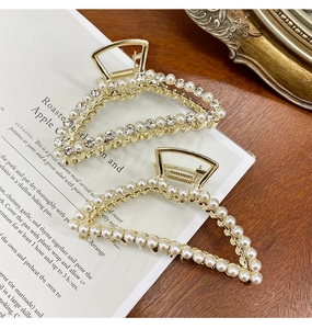 Detail of two gold metal hair claws with white pearls and rhinestones on a magazine