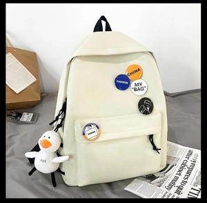 Detail of beige canvas school backpack with decorative pins and cute duck plush charm