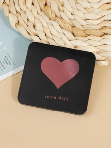 Close-up of black square compact mirror with red heart and love day text on straw mat