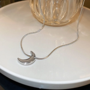 Minimalist silver crescent moon pendant necklace on a sleek snake chain displayed on ceramic