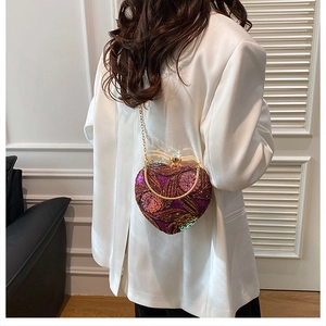 Detail of heart-shaped evening bag with purple sequins and floral embroidery on a white blazer