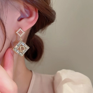 Primo piano di orecchini con perle e strass con design a lettera D su una modella