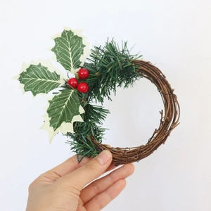 Gros plan d'une couronne de Noël rustique avec houx et baies rouges tenue à la main