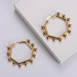 Detailed macro shot of golden hexagonal earrings with small beads on white geometry stone