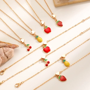Dettaglio di ciondoli a forma di frutta dorata come fragola e ananas su collane e bracciali