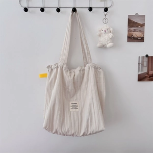 Detail of off-white pleated canvas tote bag with yellow label and minimalist texture