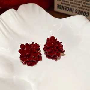 Deep red pleated flower stud earrings in high-gloss finish on a white ceramic tray