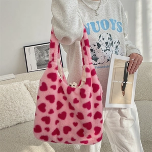 Detail of pink faux fur tote bag featuring red heart patterns in a cozy home setting