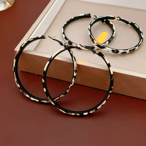 Detail shot of leopard and snake print leather hoop earrings on a beige display tray
